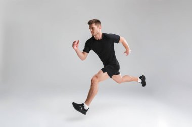 Tam uzunlukta portresi hızlı izole gri arka plan üzerinde çalışan bir kendine güvenen genç sporcu