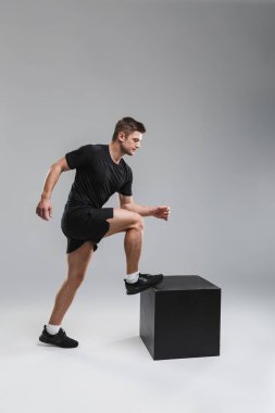 Güçlü bir genç sporcu gri arka plan üzerinde izole bir blok üzerinde adım tam uzunlukta portresi