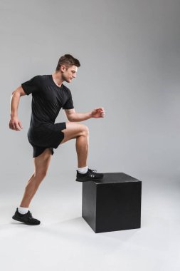 Konsantre bir genç sporcu gri arka plan üzerinde izole bir blok üzerinde adım tam uzunlukta portresi