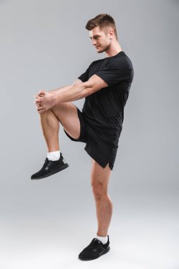 Gri arka plan üzerinde izole germe egzersizleri yapıyor odaklı bir genç sporcu portresi