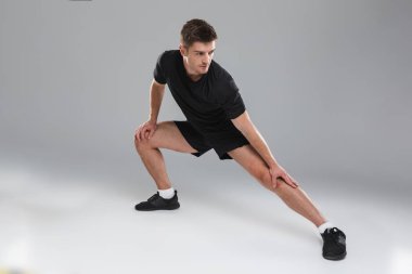 Gri arka plan üzerinde izole germe egzersizleri yapıyor sağlıklı bir genç sporcu portresi