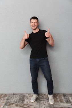 Tam uzunlukta başparmak gri arka plan üzerinde izole gösteren genç gülümseyen bir adam portresi