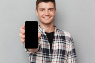 Boş ekran cep telefonu gri arka plan üzerinde gösterilen kendine güvenen genç bir adam portresi