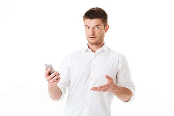 Portrait Confused Young Man Holding Mobile Phone Isolated White Background — Stock Photo, Image