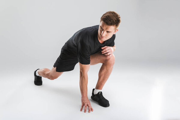 Portrait of a motivated young sportsman doing stretching exercises isolated over gray background