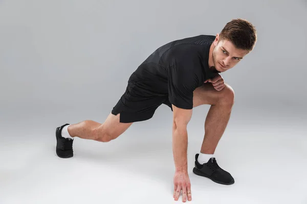 灰色の背景の上分離したストレッチ体操を行う集中若いスポーツマンの肖像画 — ストック写真