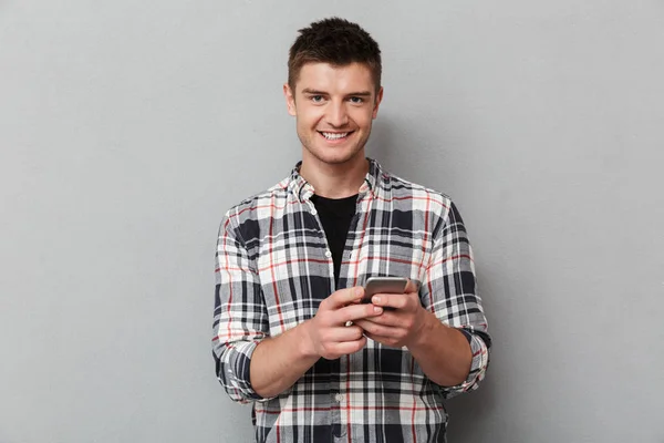 在灰色背景下手持手机的微笑年轻人的肖像 — 图库照片