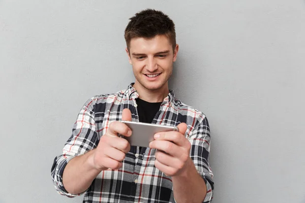 Retrato Joven Sonriente Jugando Juegos Teléfono Móvil Sobre Fondo Gris — Foto de Stock