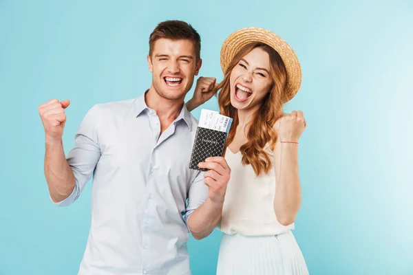 stock image Image of young happy caucasian loving couple isolated over blue background holding passport with tickets make winer gesture.