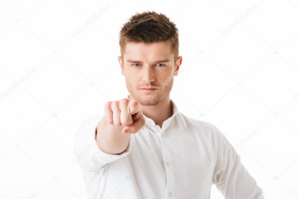 Portrait of a serious young man pointing finger at camera isolated over white background