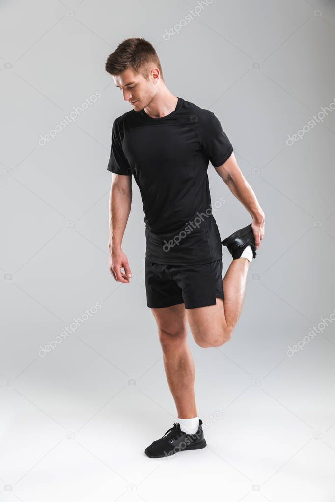 Portrait of a smiling young sportsman doing stretching exercises isolated over gray background