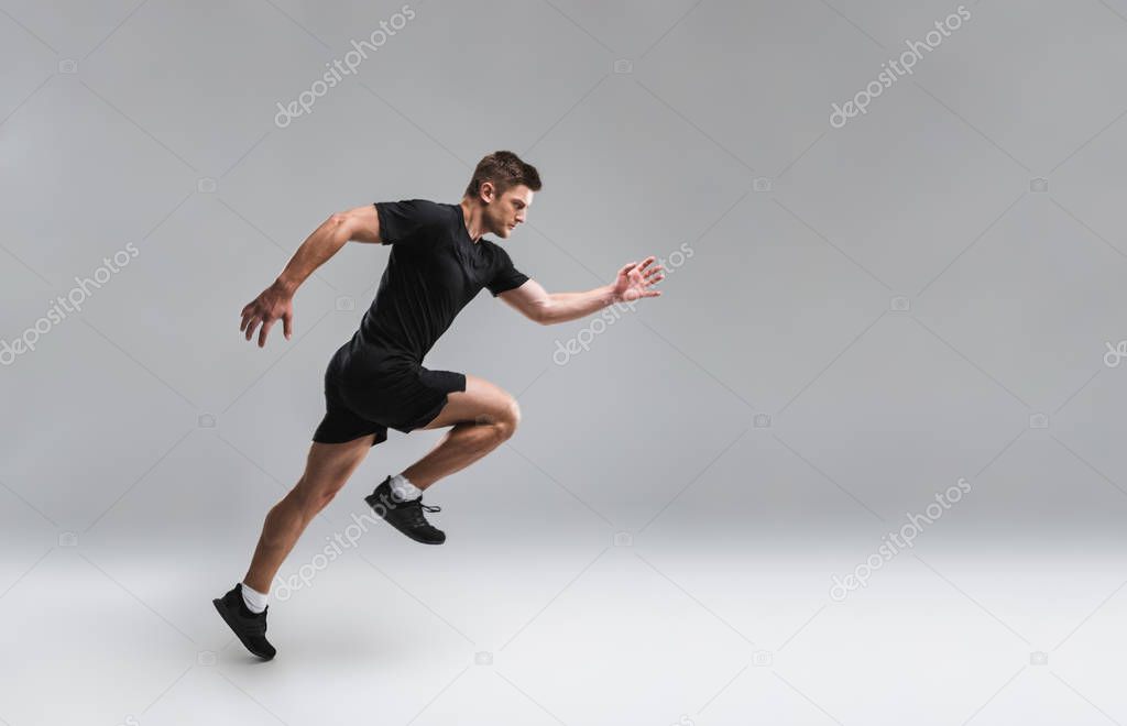 Full length portrait of a focused young sportsman running fast isolated over gray background