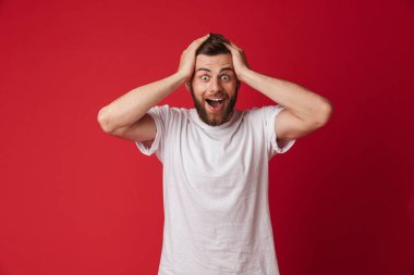 Şok genç yakışıklı adam kırmızı duvar arka plan üzerinde izole ayakta resmi. Görünümlü kamera.