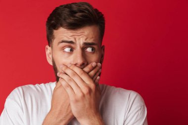 Görüntü izole kırmızı duvar arka plan üzerinde duran ellerle ağız kapsayan korkmuş genç adam.
