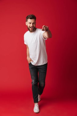 Fotoğraf izole kırmızı duvar arka plan üzerinde yürüme yakışıklı genç adamın. Kenara işaret arıyorum.