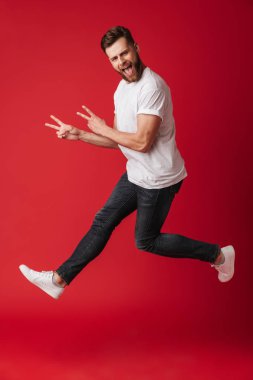 Barış hareketi gösterilen Kırmızı duvar arka plan üzerinde izole fotoğraf yakışıklı genç adamın atlama.