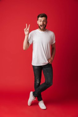 Görüntü izole kırmızı duvar arka plan üzerinde duran mutlu yakışıklı genç. Kamera gösteren barış hareketi arıyorsunuz.