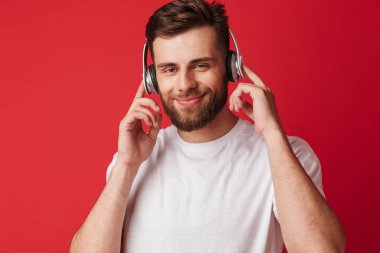 Yakışıklı genç adamın kulaklık ile müzik dinleme kırmızı duvar arka plan üzerinde izole fotoğraf.