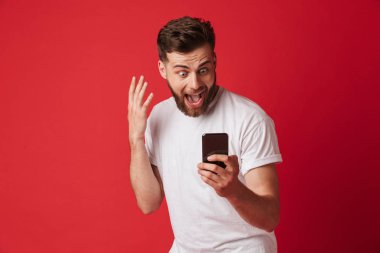 Cep telefonu kullaranarak kırmızı duvar arka plan üzerinde izole ayakta genç adam çığlık fotoğrafı şok.