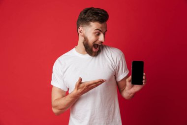 Heyecanlı genç adam cep telefonu görüntüsünü gösterilen Kırmızı duvar arka plan üzerinde izole ayakta görüntüsünü.