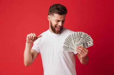 Heyecanlı genç adam para işaret tutan kırmızı duvar arka plan üzerinde izole görüntüsünü.