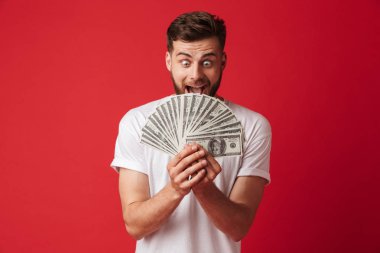 Heyecanlı çığlık atan genç adam para tutan kırmızı duvar arka plan üzerinde izole görüntüsünü.