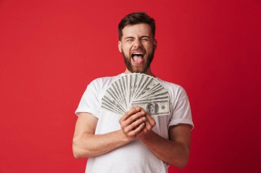 Heyecanlı çığlık atan genç adam para tutan kırmızı duvar arka plan üzerinde izole görüntüsünü.