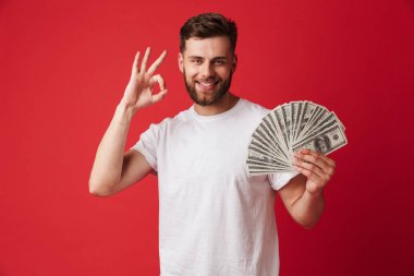 İyi jest yapmak imge-in para tutan kırmızı duvar arka plan üzerinde izole heyecanlı genç adam.