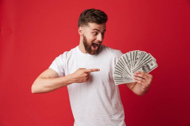 Heyecanlı genç adam para işaret tutan kırmızı duvar arka plan üzerinde izole görüntüsünü.