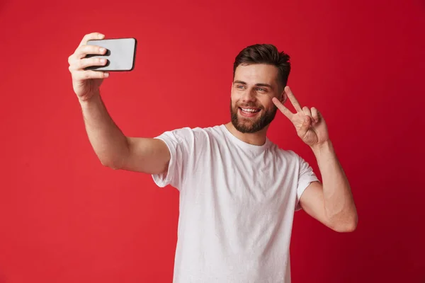 赤い壁の背景に分離立って幸せな若い男のイメージする平和のジェスチャーによって携帯電話 Selfie — ストック写真