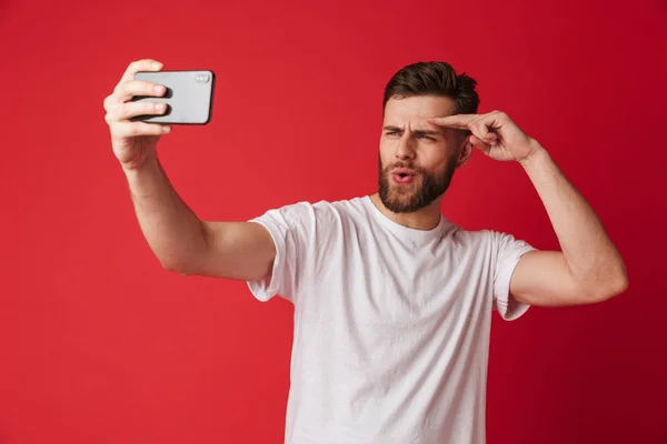 分離赤い壁の背景の上に立っている感情的な若い男の画像が携帯電話で Selfie を作る — ストック写真