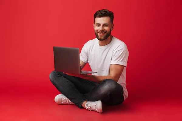 Imagem Jovem Feliz Sentado Isolado Sobre Fundo Parede Vermelha Usando — Fotografia de Stock