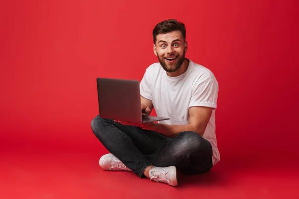 Imagem Jovem Feliz Sentado Isolado Sobre Fundo Parede Vermelha Usando — Fotografia de Stock