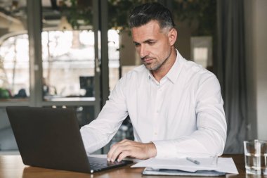 Ofiste tabloda çalışmaları sırasında belgeleri ve dizüstü bilgisayar ile oturup konsantre emin işadamı 30'lu giyen beyaz gömlek görüntü