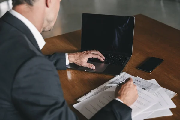 功利的な男が身に着けている白いシャツと黒いスーツ オフィスでテーブルに座っていると 文書で作業中にノート パソコンを見て裏からの画像 — ストック写真