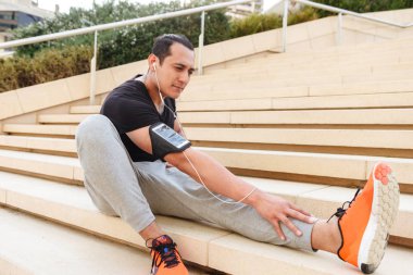 Yakışıklı genç sporcu germe yapıyor portresi kulaklık mekanlarda egzersizleri.