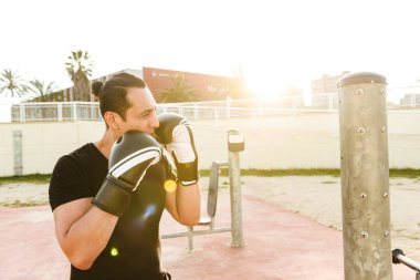 Güçlü yakışıklı genç sporcu boxer eldiven fotoğraf olun açık havada bir kenara seyir egzersizleri.