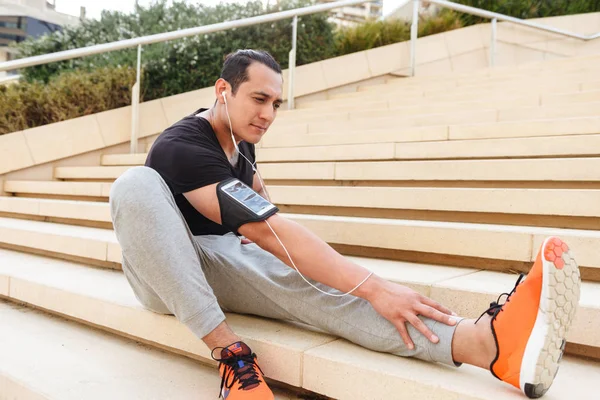 Yakışıklı genç sporcu germe yapıyor portresi kulaklık mekanlarda egzersizleri.