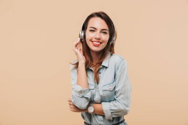 Mutlu kadın kamera seyir bej arka plan duvardan izole müzik ayakta dinlerken kulaklık görüntüsünü.