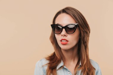 Görüntü oldukça genç ciddi kadının bej arka plan duvar bir yana bakmaktan izole duran güneş gözlüğü takıyor.