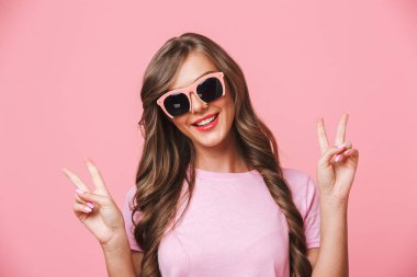 Görüntü closeup kafkas kadın kameraya gülümseyen ve barış işareti iki elle izole pembe arka plan üzerinde gösterilen lüks güneş gözlüğü takıyor