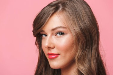 Avrupa 20'li yaşlarda olan kadın uzun kıvırcık saç modeli ve akşam makyaj pembe arka plan üzerinde izole baştan çıkarıcı bakışla kameraya gülümseyen resim closeup