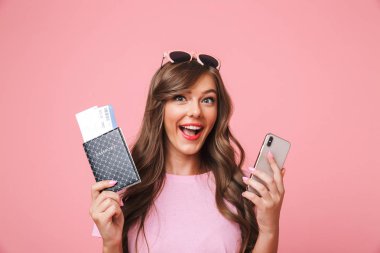Başarılı yolculuk kız 20'li yaşlarda ifade zevk passport uçak bileti ve smartphone ile pembe arka plan üzerinde izole elinde tutarken görüntüsünü