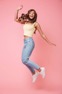 Mutlu pembe arka plan üzerinde sevindirici ve atlama uzun kahverengi saçlı neşeli kadın fotoğrafı tam uzunlukta izole