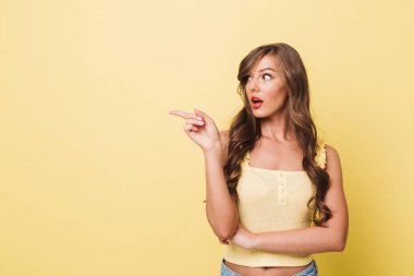 Sürpriz kadın 20'li yaşlarda boşaltmak izole sarı arka plan üzerinde bir kenara parmakla rahat giyim uzun kahverengi saçlı fotoğrafı
