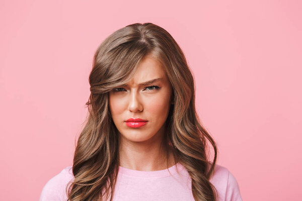 Photo closeup of upset woman with long curly hair in basic t-shirt pouting and frowning in resentment isolated over pink background