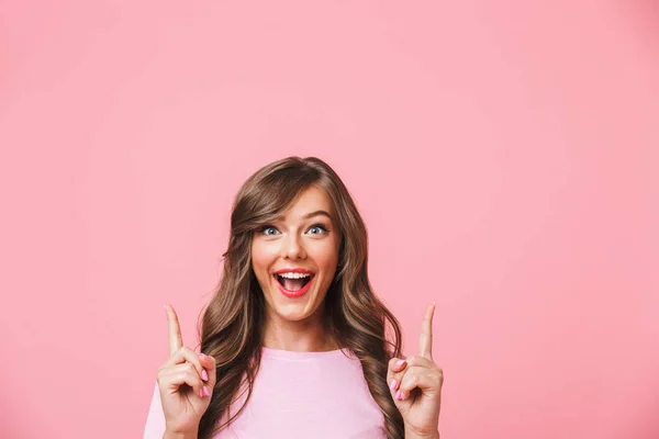 ピンクの背景に分離されたロングカーリー茶髪ポインティング指 Copyspace を上方とうれしそうなきれいな女性をクローズ アップ — ストック写真