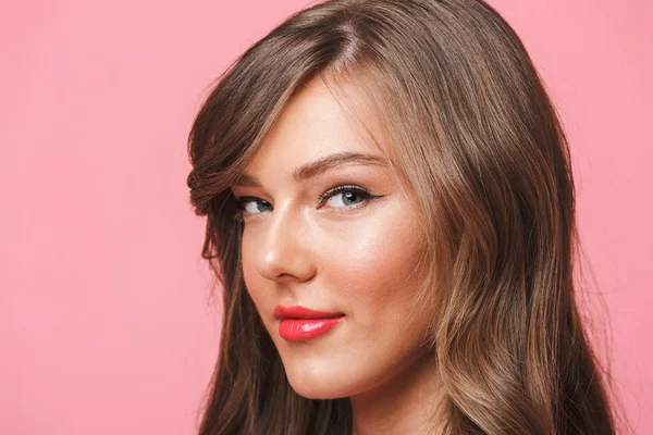 Avrupa 20'li yaşlarda olan kadın uzun kıvırcık saç modeli ve akşam makyaj pembe arka plan üzerinde izole baştan çıkarıcı bakışla kameraya gülümseyen resim closeup