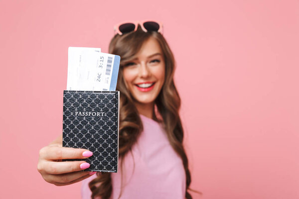 Image of joyful beautiful woman in casual clothing showing passport and air tickets at camera isolated over pink background