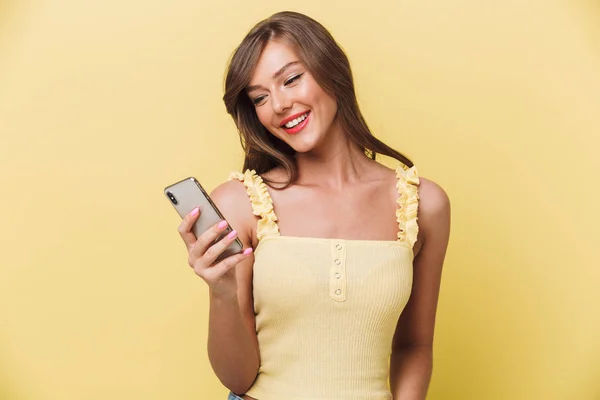一个快乐的年轻女孩的肖像看着手机在黄色背景下隔离 — 图库照片